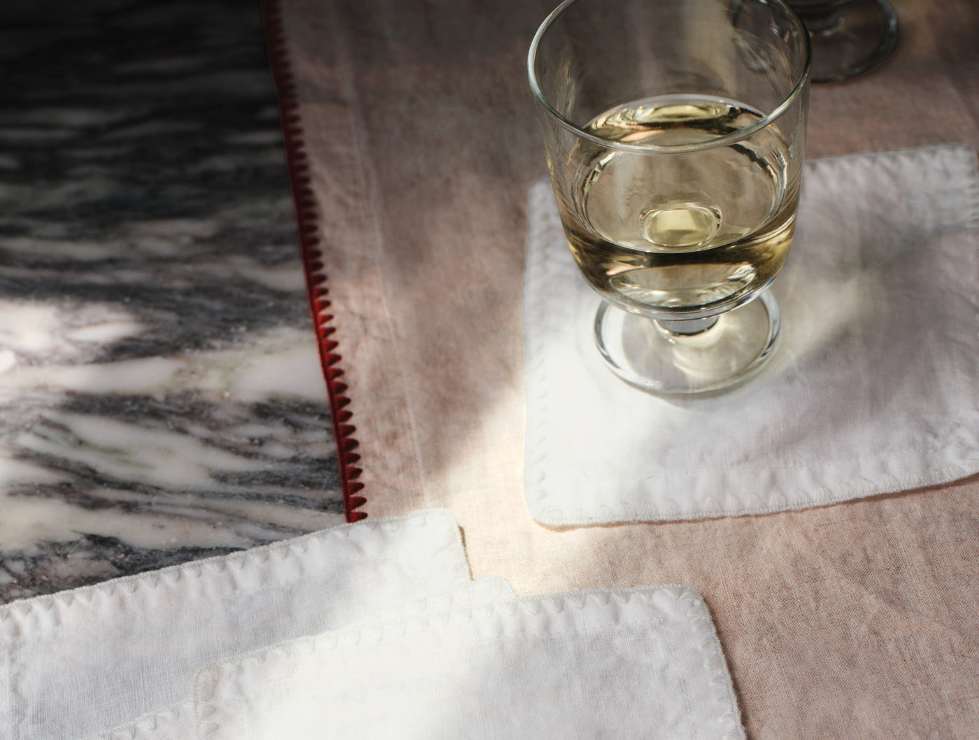 White linen napkin on marble surface, red embroidered edge detail, styled with wine glass.