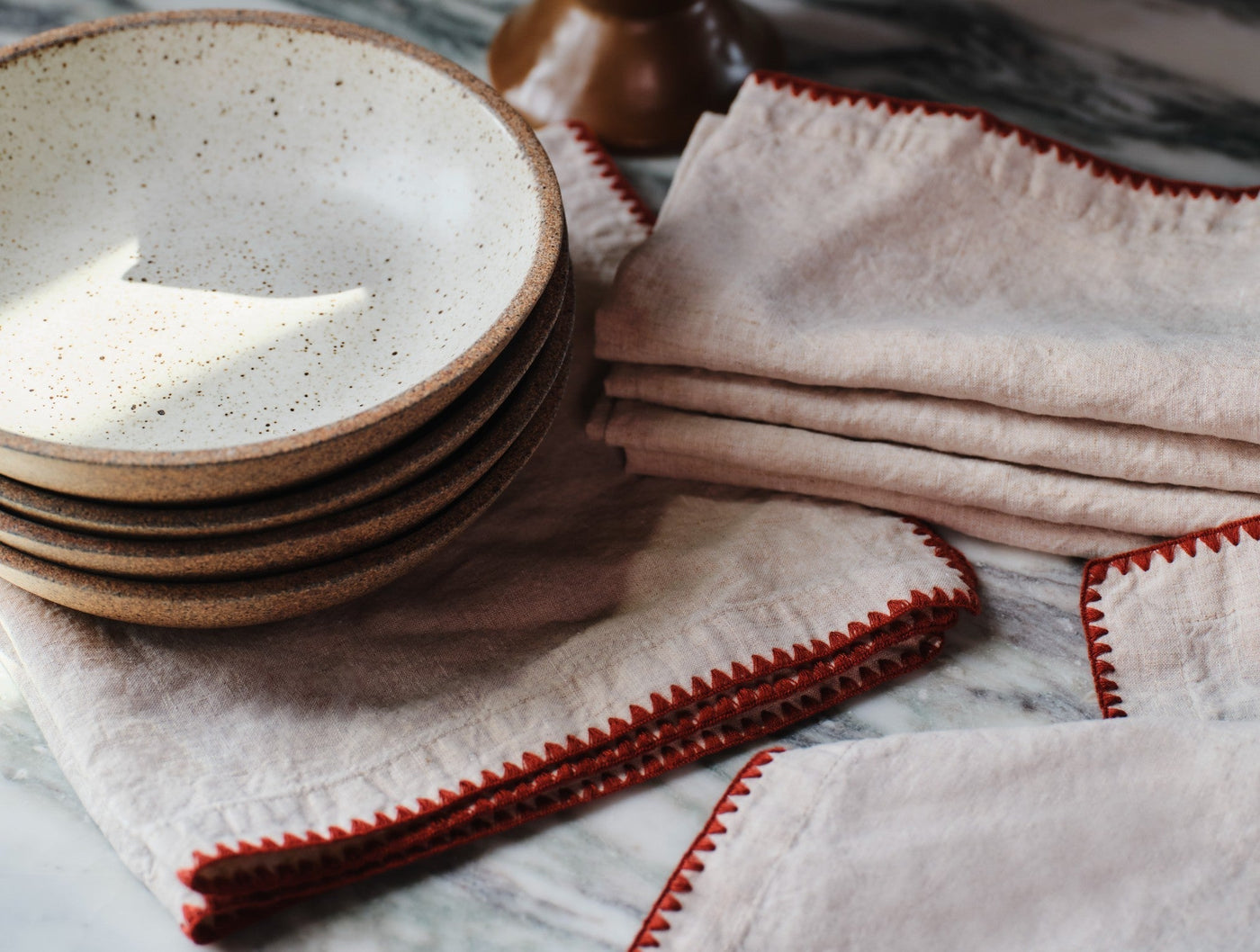 Blush linen cocktail napkins with red blanket-stitch embroidered edges, styled with stacked ceramic bowls.