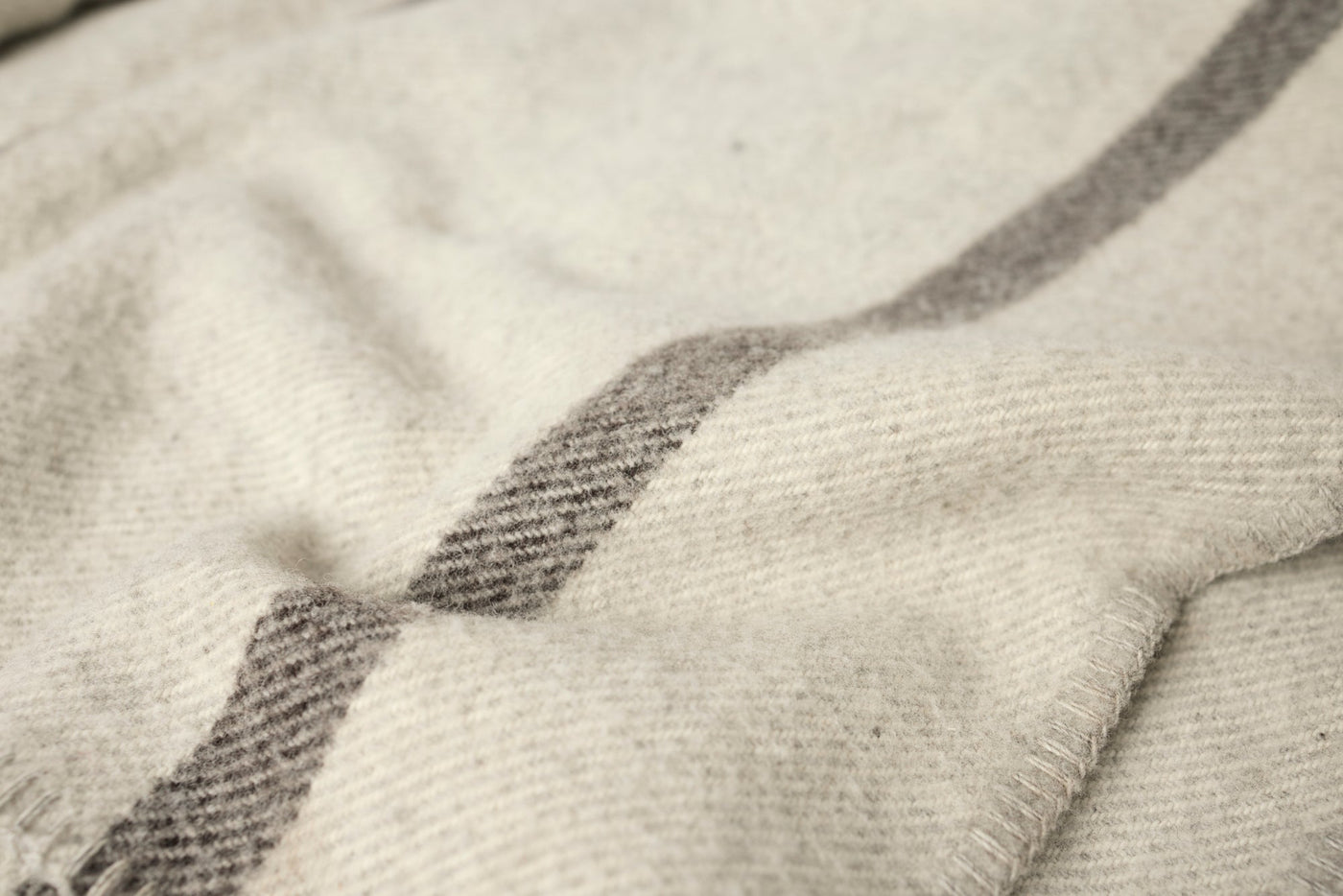 Close-up of ivory wool blanket weave with grey stripe detail and fringe edge.