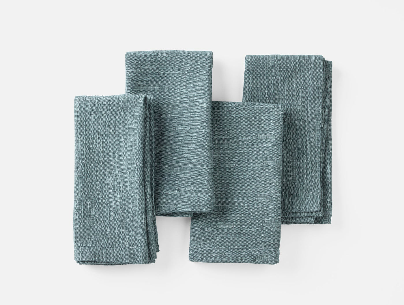 Four folded Coyuchi Toro Canyon napkins in slate blue linen, arranged in a flat lay on white.