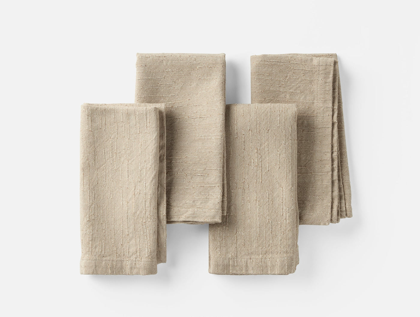 Four folded Coyuchi Toro Canyon linen napkins in natural tan, arranged flat on white surface.
