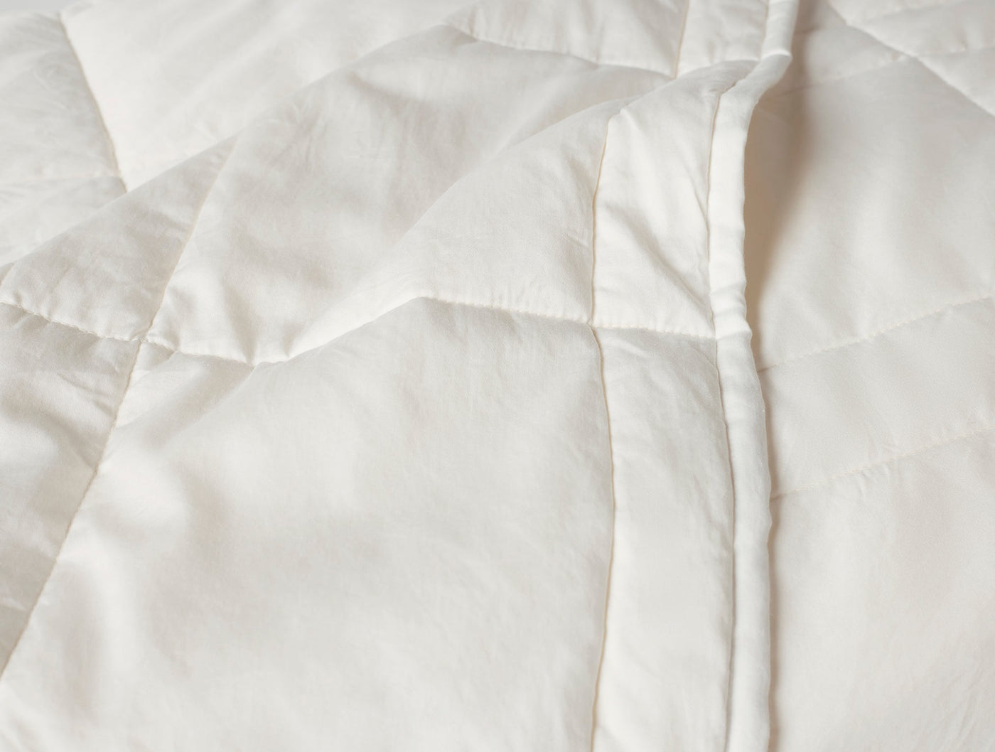 Close-up of ivory quilted comforter edge, showing baffle stitching and soft drape.