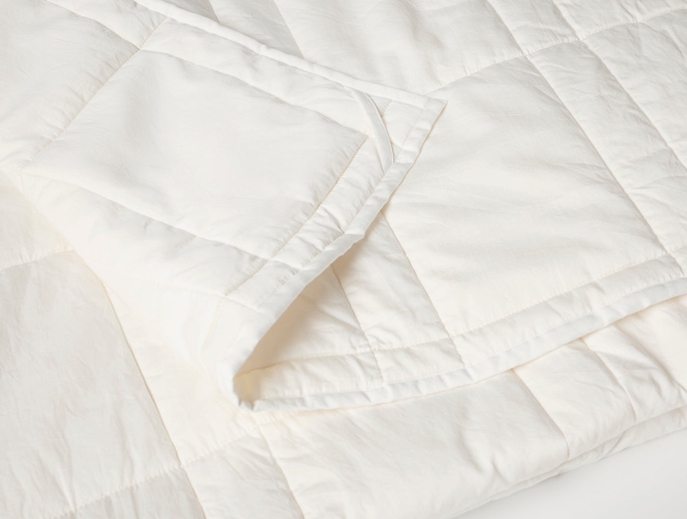 Close-up of Coyuchi ivory quilted comforter corner showing stitched diamond pattern and edge binding.