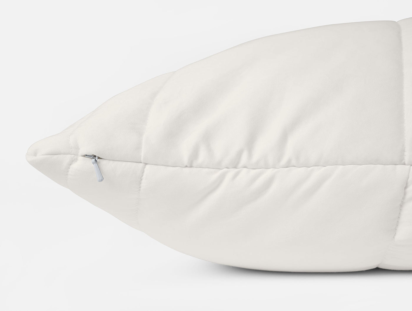 Close-up of ivory Coyuchi pillow protector corner, showing zipper closure and quilted stitching.