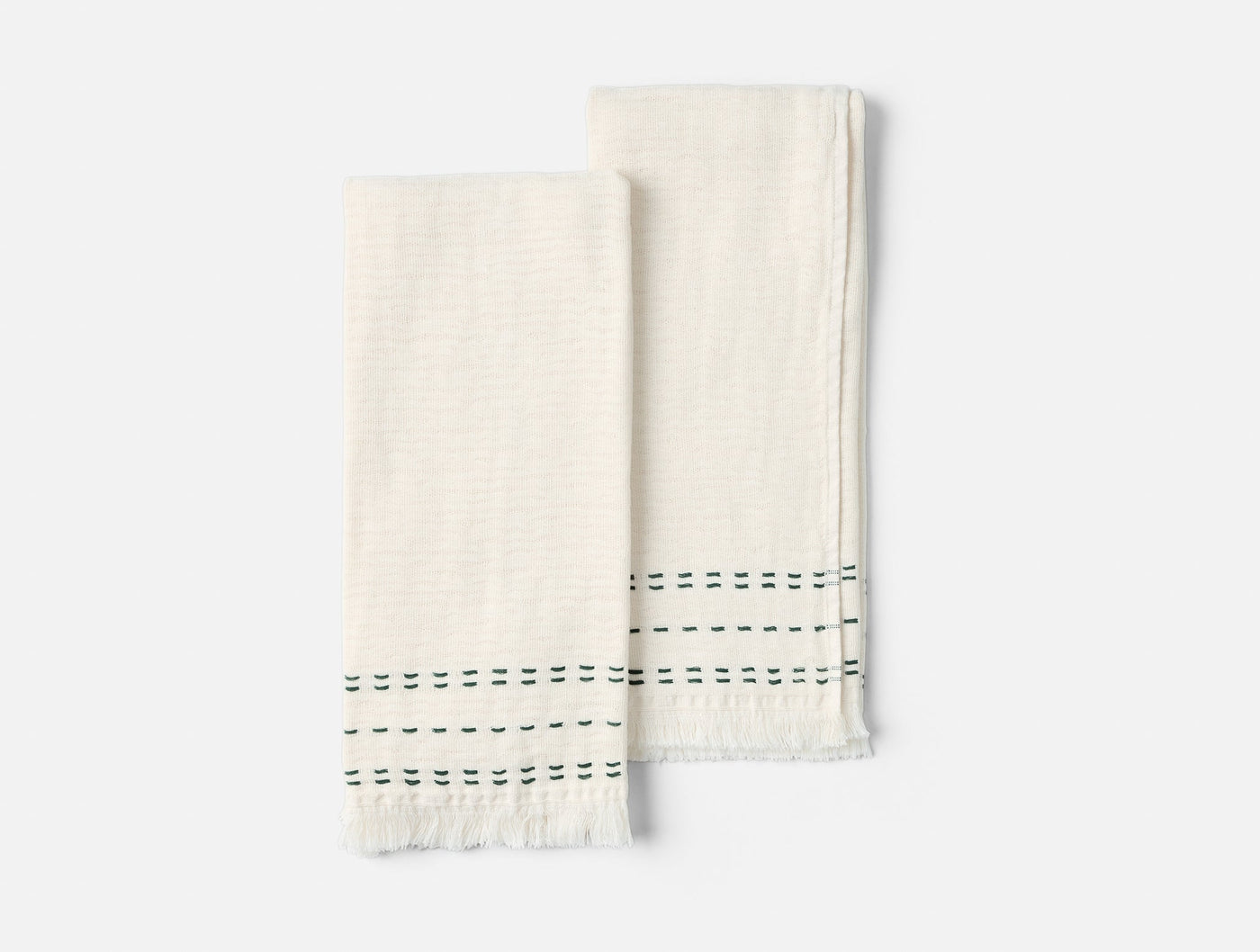Pair of ivory hand towels with green dashed stripe detail and fringe hem, flat lay view.