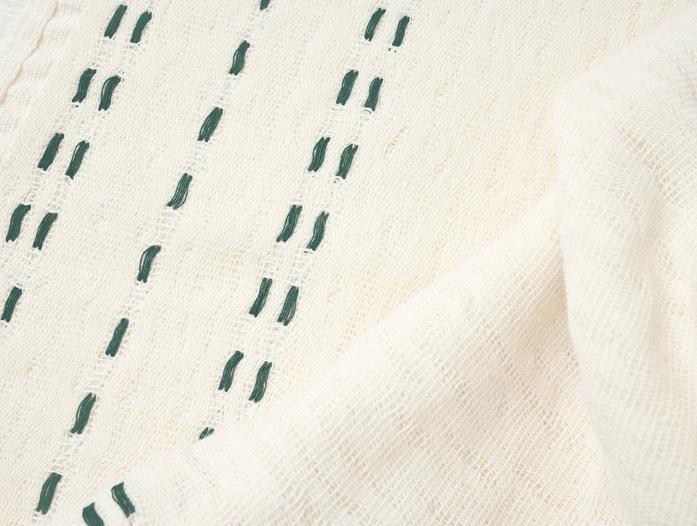 Close-up of ivory woven hand towel with forest green dash stitch detail.
