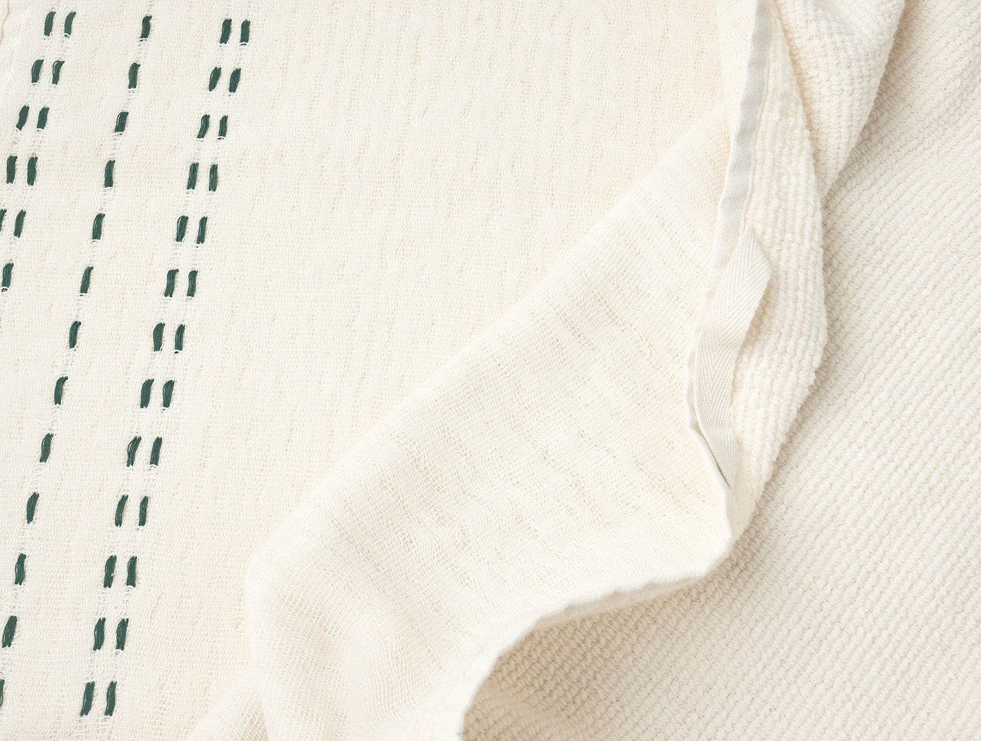 Ivory Coyuchi Alder hand towel close-up showing forest green dash embroidery and folded hem detail.
