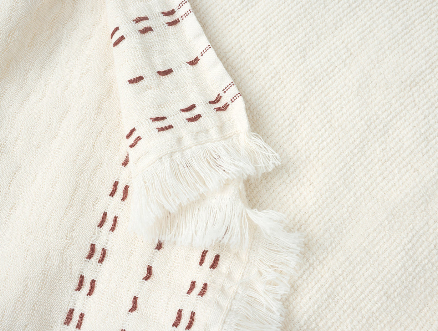 Close-up of Coyuchi Alder hand towel fringe hem with rust dash pattern on ivory cotton.