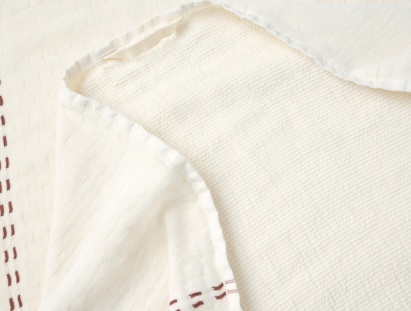 Close-up of ivory waffle-weave hand towel corner with burgundy hem stitching detail.