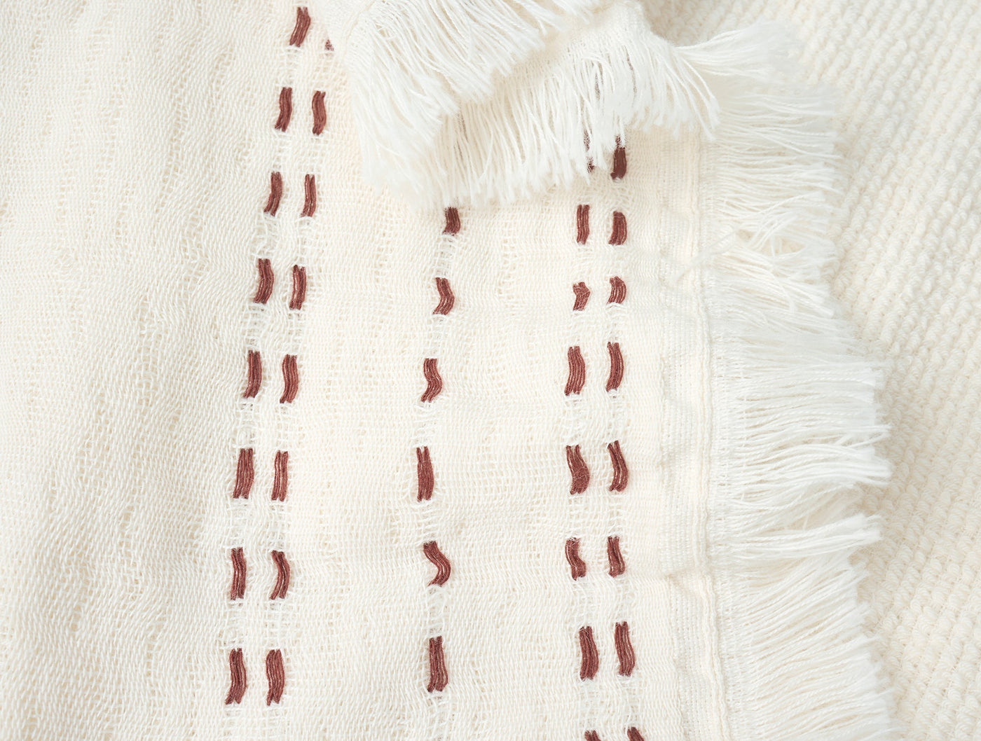 Close-up of Coyuchi Alder hand towel fringe edge with terracotta dash embroidery on ivory cotton.