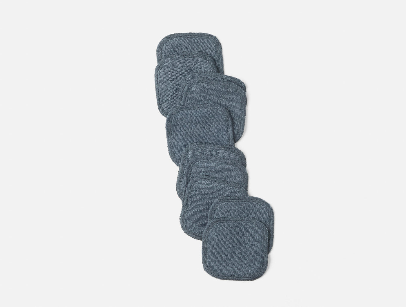 Eight slate blue Coyuchi Bare makeup pads arranged in a diagonal stack on white background.