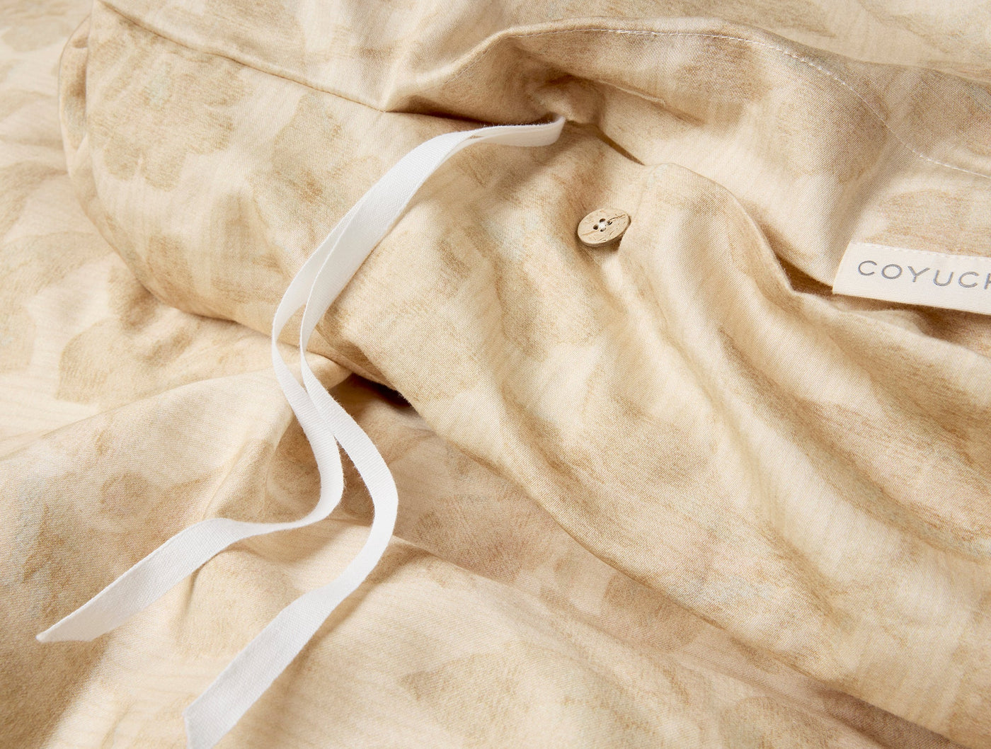 Close-up of Coyuchi Camellia duvet cover showing coconut button closure and white ties in sand.