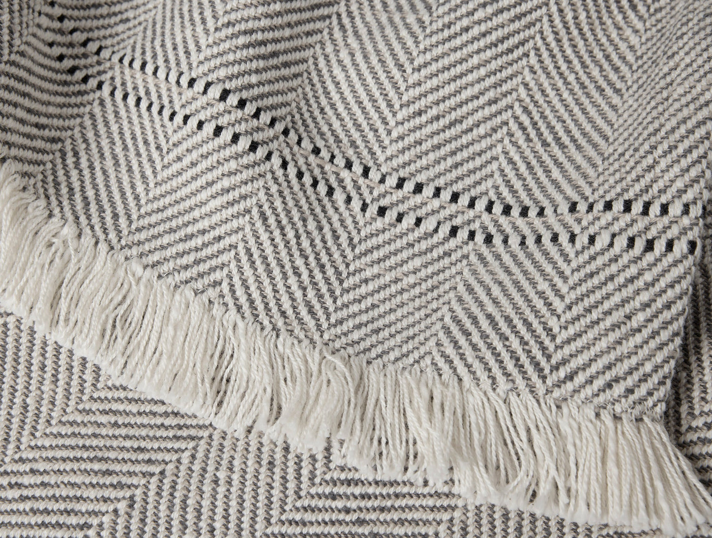Close-up of Coyuchi Canyon throw fringe and grey herringbone weave detail.