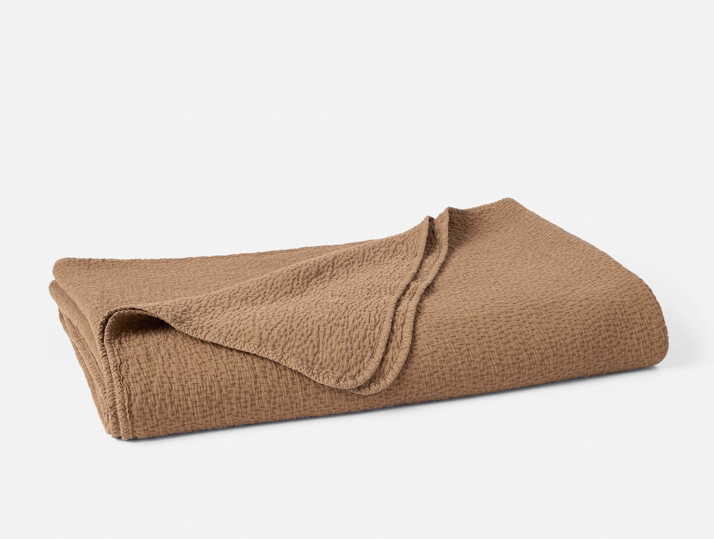 Folded caramel matelassé blanket showing textured weave pattern on rounded corners.