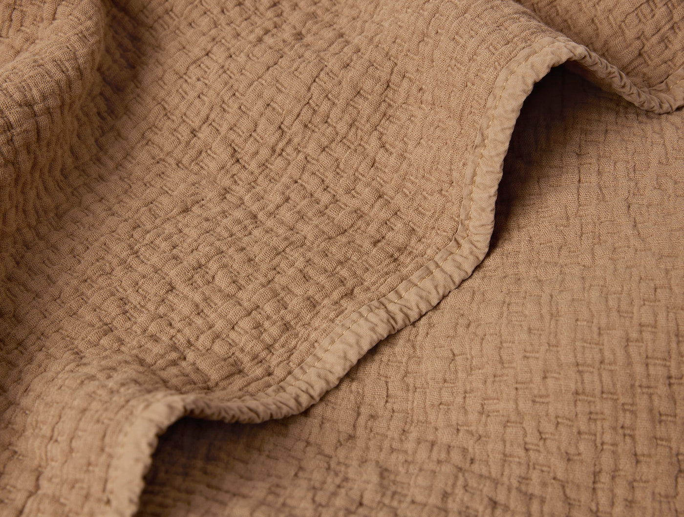 Close-up of Coyuchi Cascade Matelassé blanket in camel, showing textured woven surface.