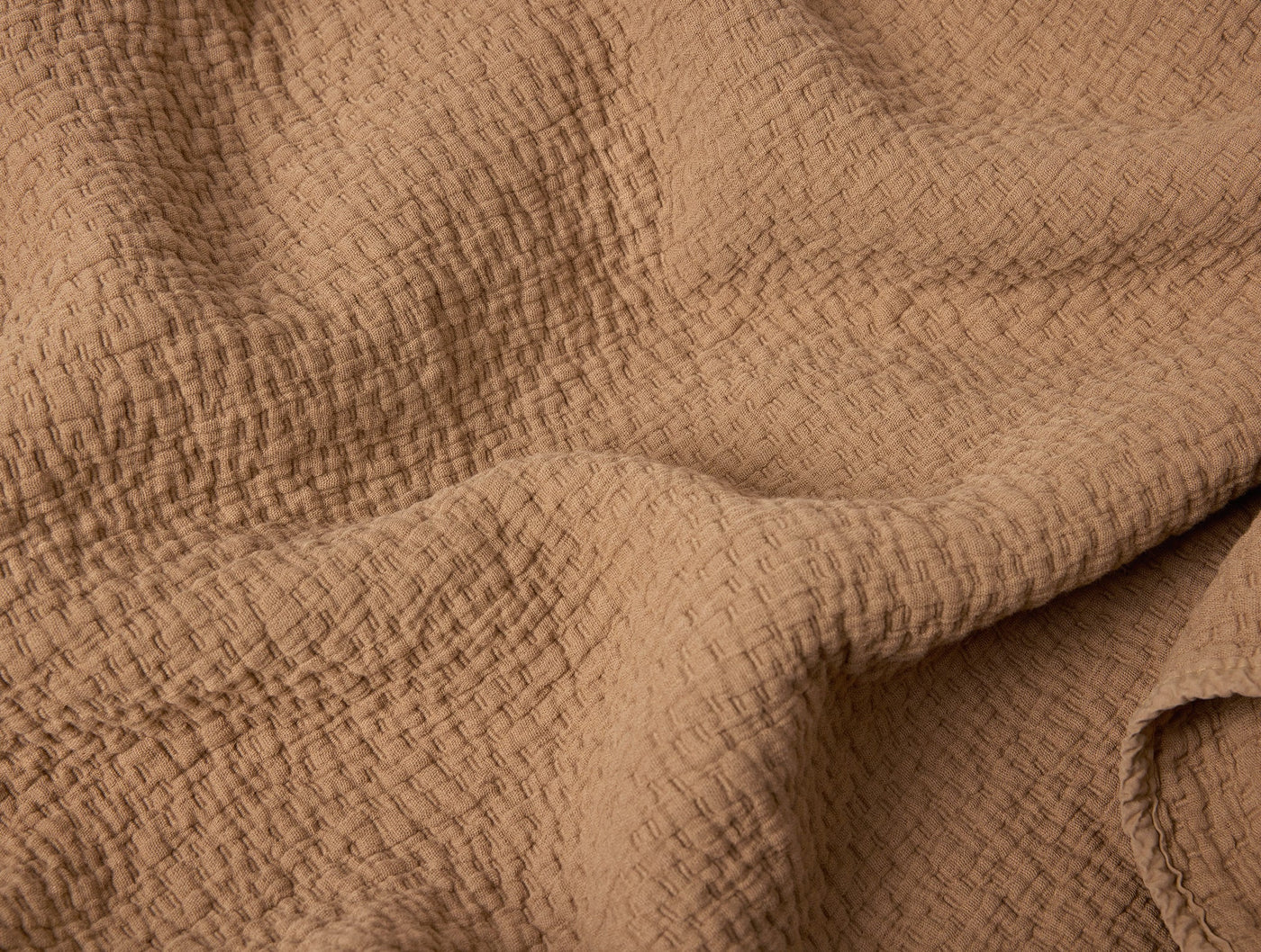 Close-up of Coyuchi Cascade Matelasse blanket in camel, showing woven texture and soft drape.
