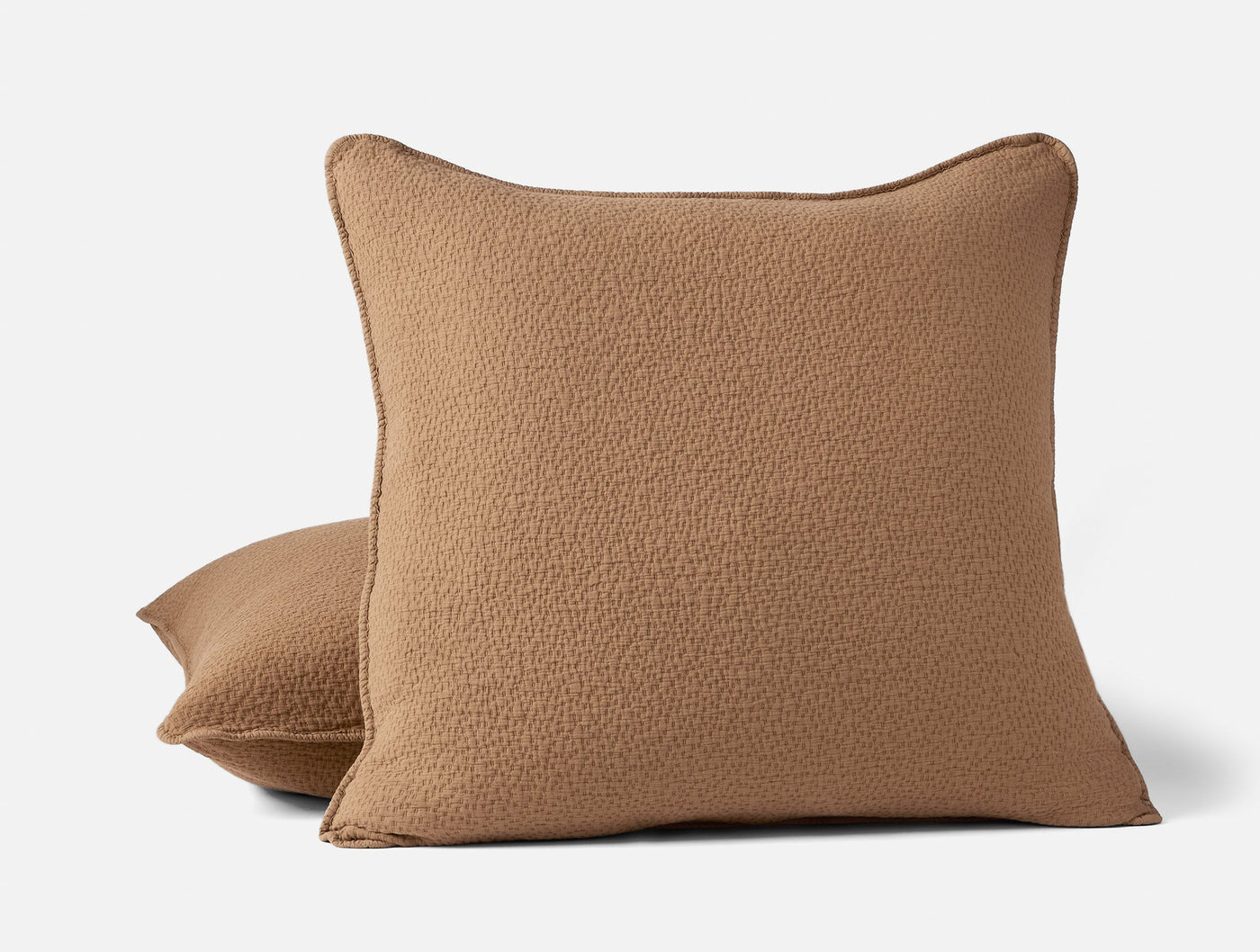 Close-up of two stacked camel matelassé pillow shams with textured weave and contrast trim.