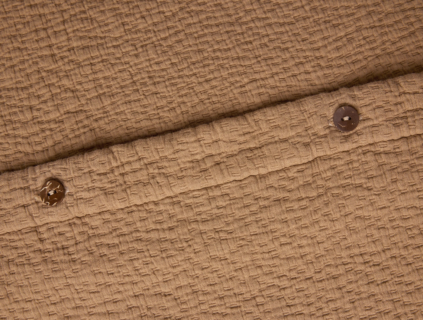 Close-up of Coyuchi Cascade Matelassé sham in camel, showing button closure and textured weave.