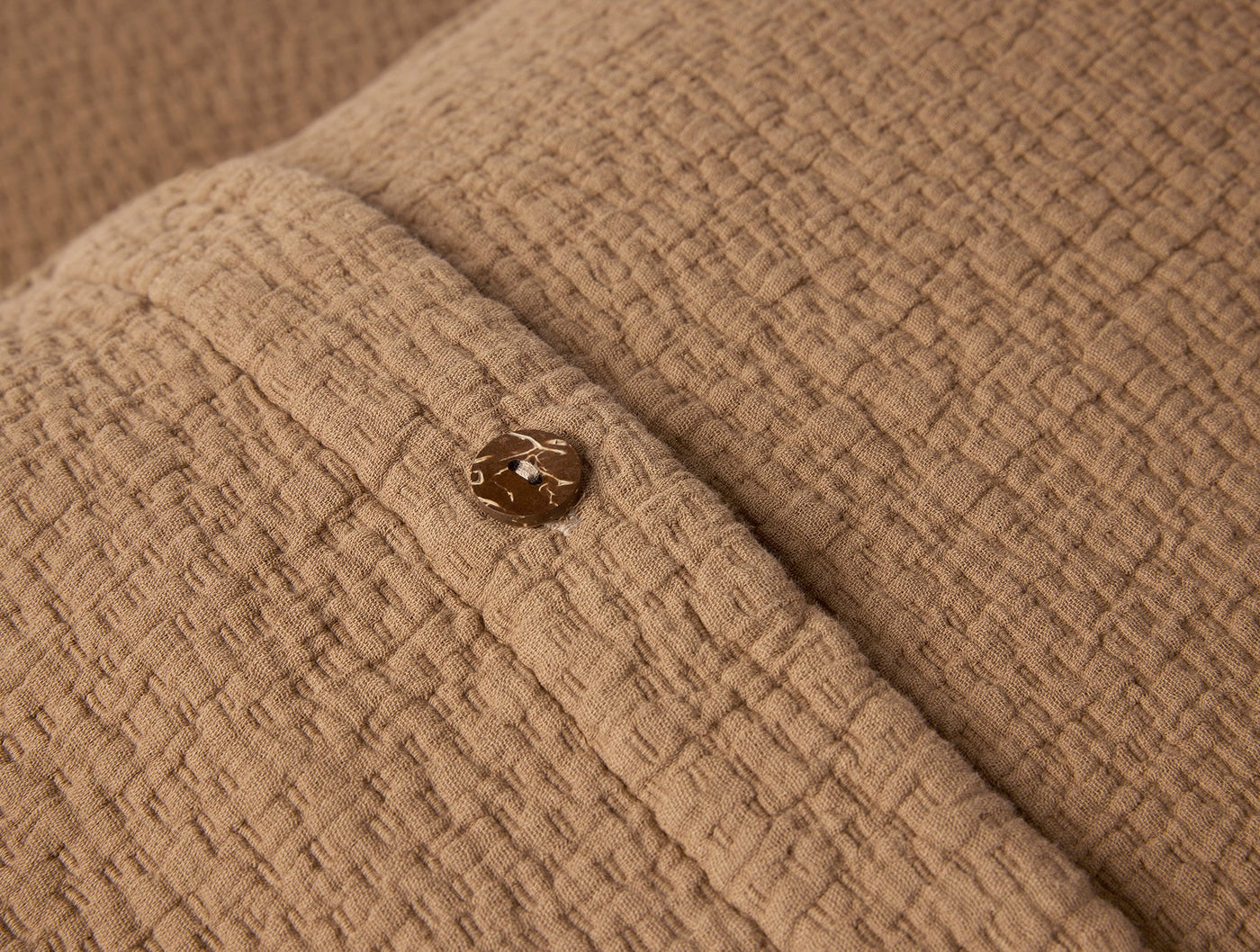 Close-up of Coyuchi Cascade Matelassé sham in warm tan, showing gold button closure detail.