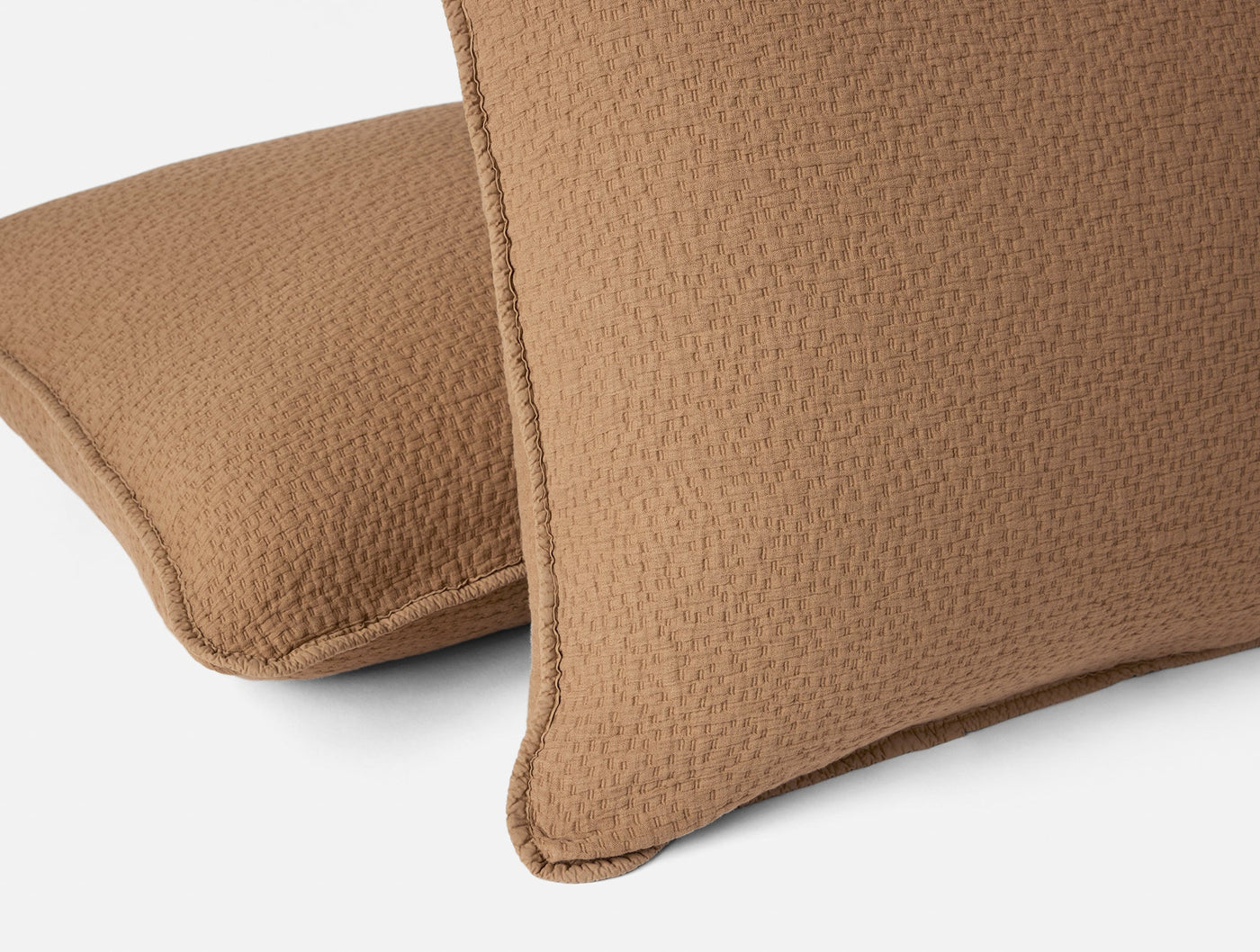 Close-up of two Coyuchi Cascade Matelassé shams in warm camel with textured weave detail.