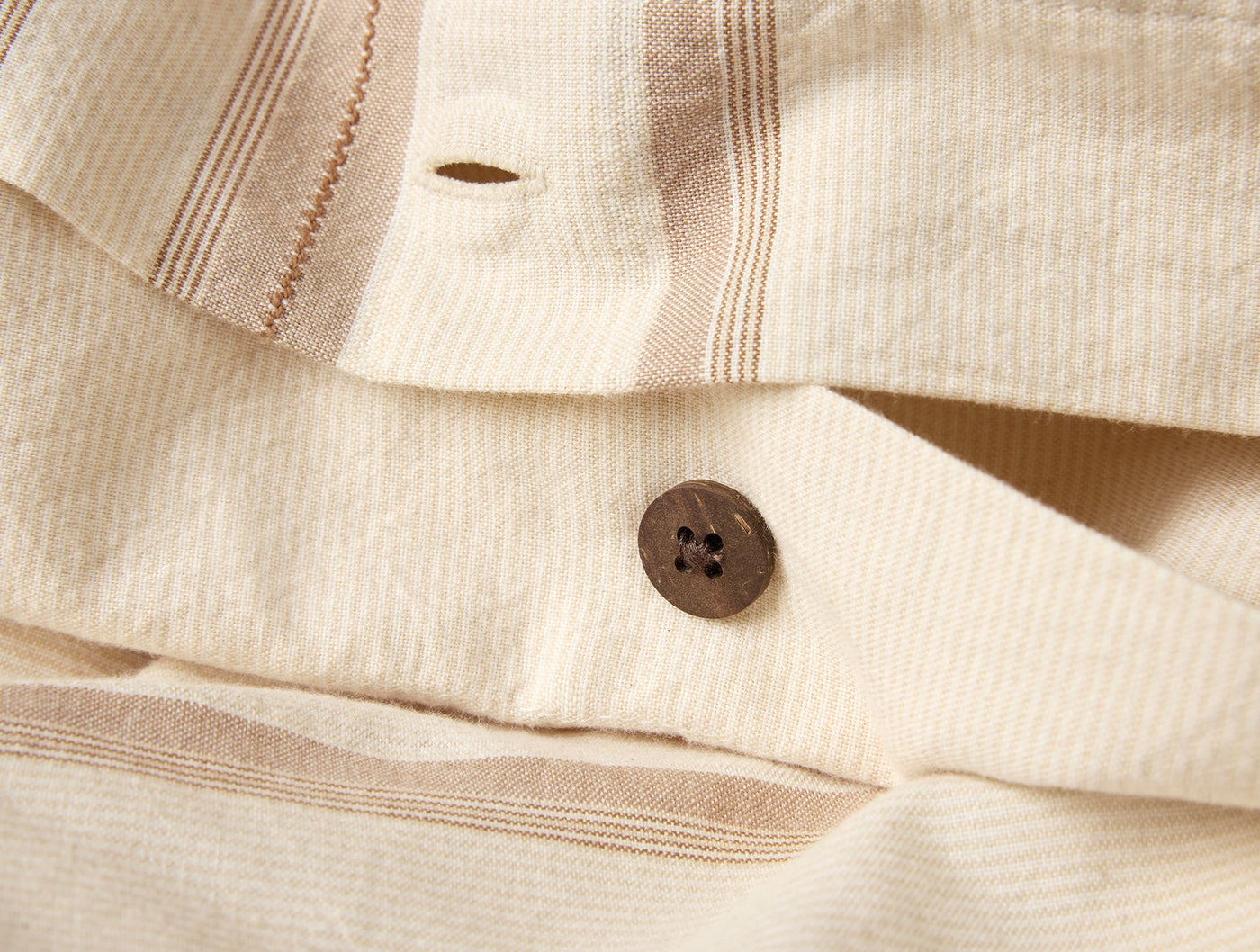 Close-up of dark brown coconut shell button closure on ivory striped linen duvet cover.