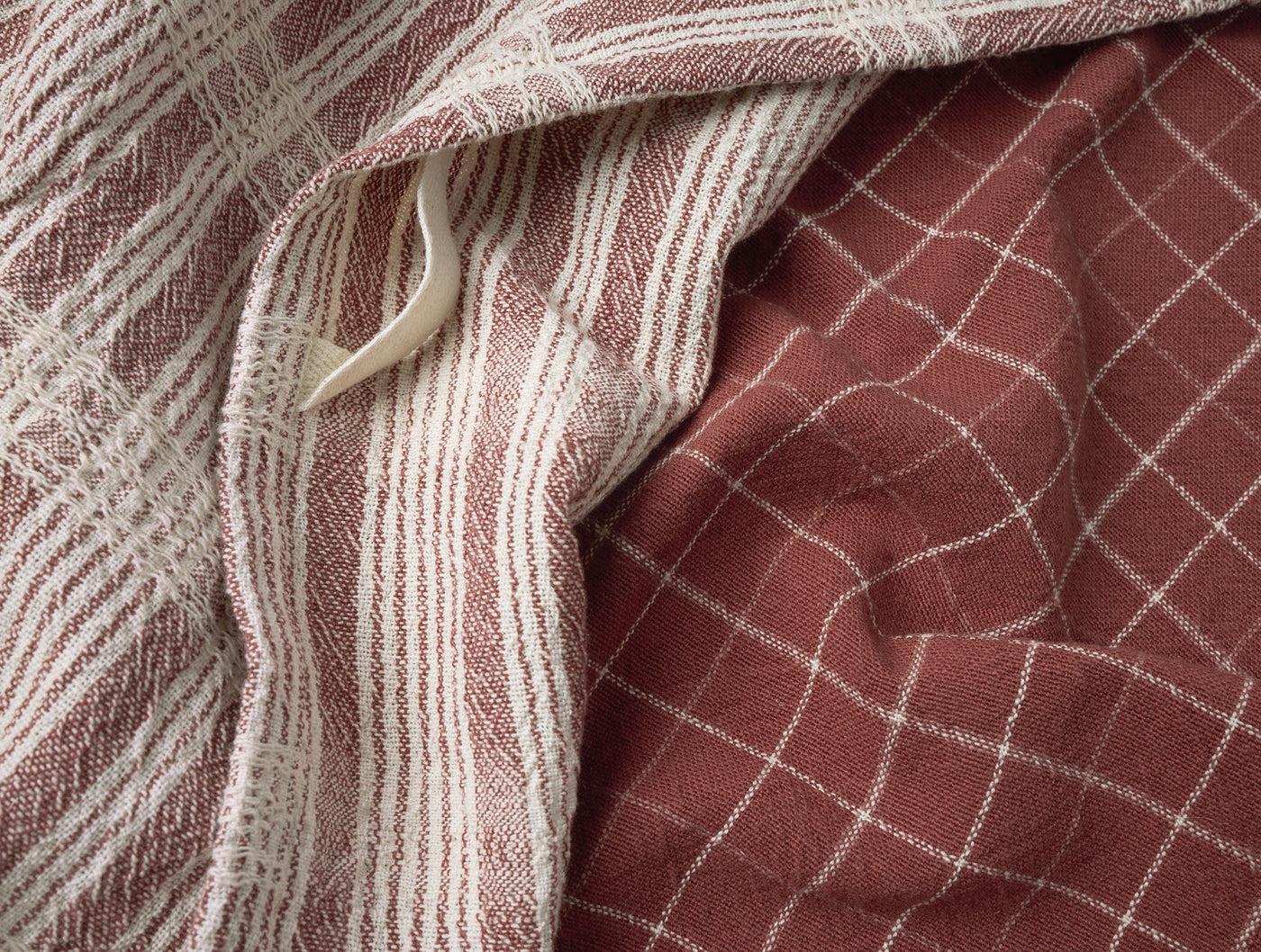 Close-up of Coyuchi Clarendon kitchen towels in terracotta, showing grid and stripe weave patterns.