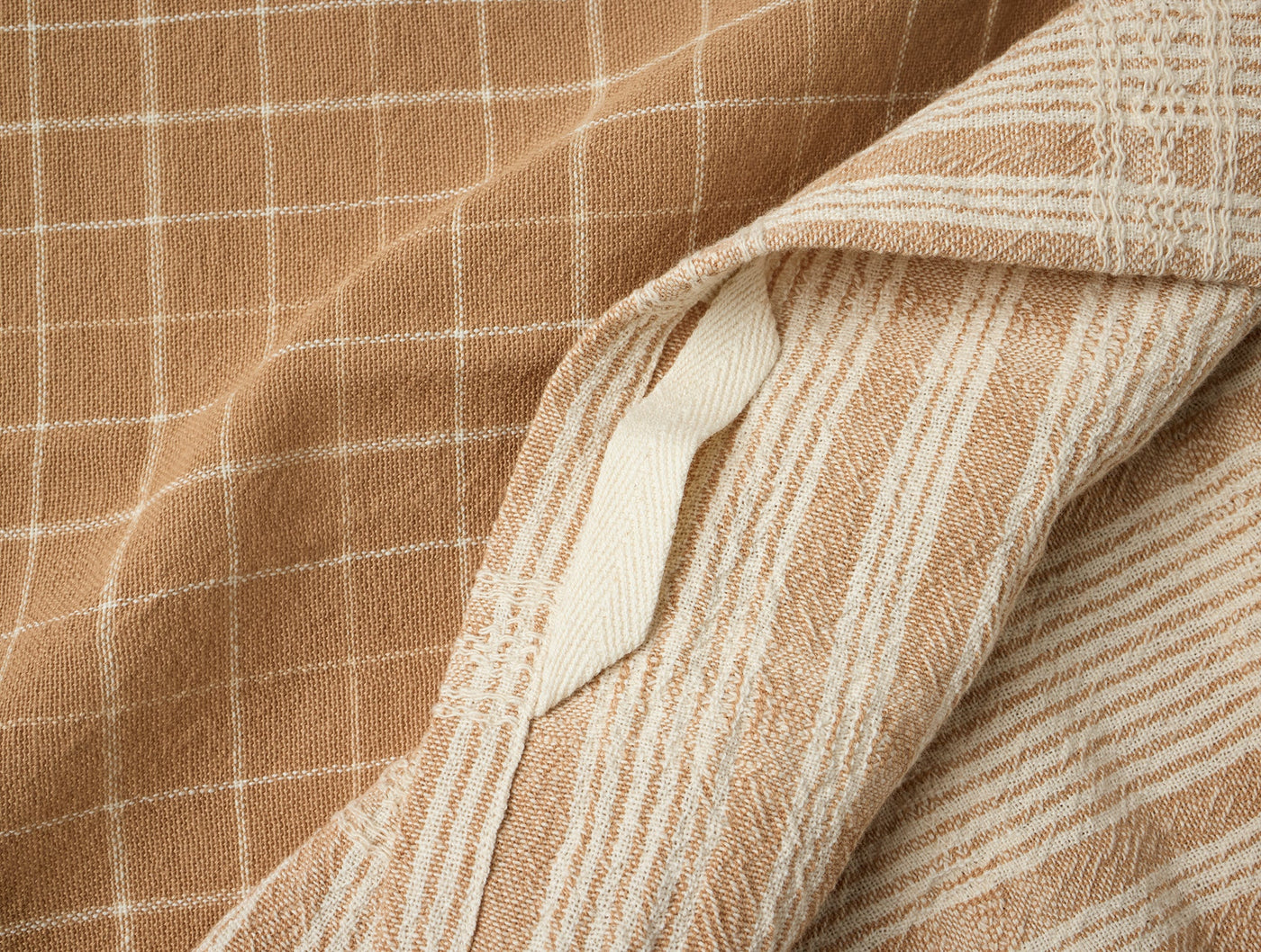 Close-up of camel and ivory woven check and stripe patterns with button closure detail.
