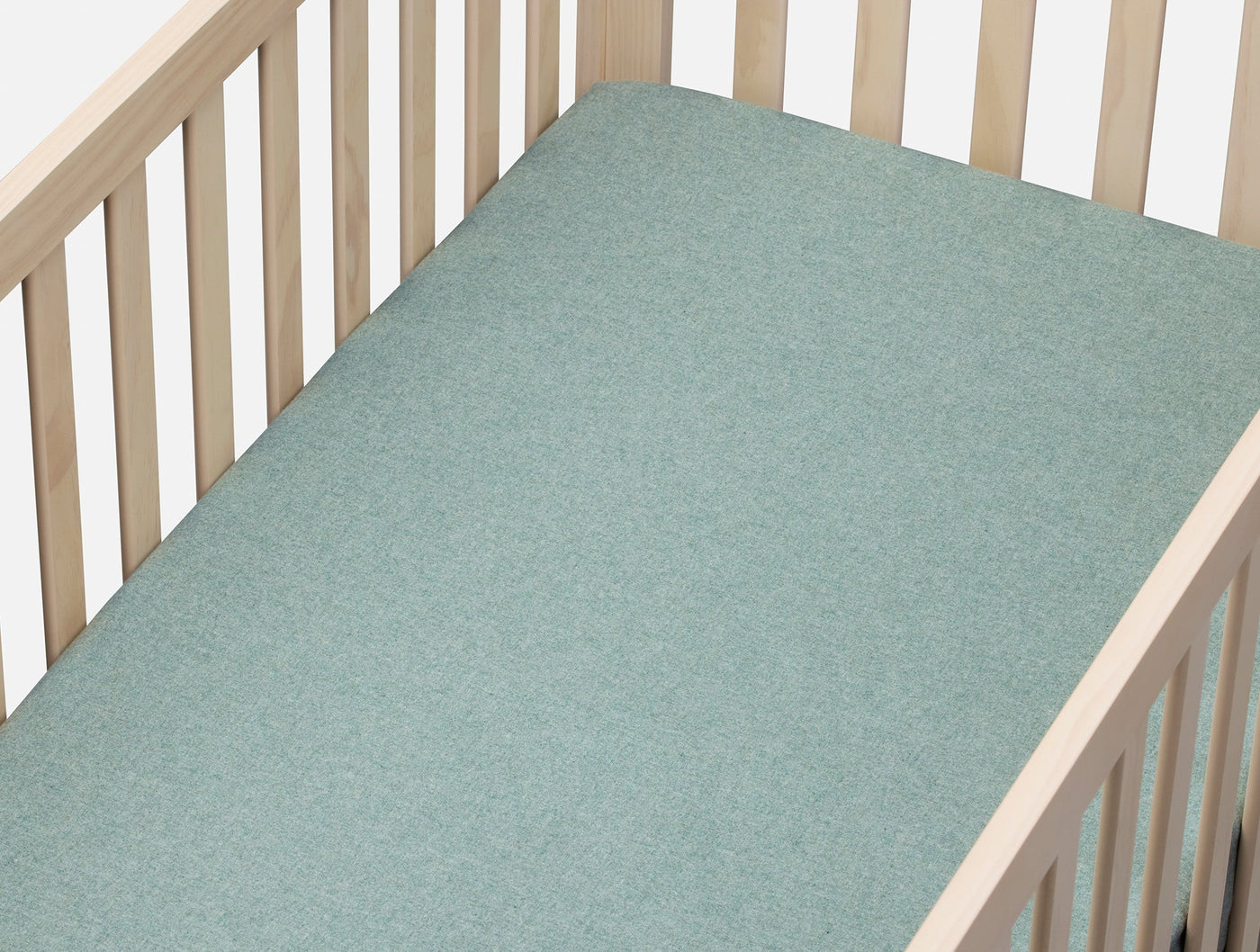 Sage green flannel fitted sheet on a natural wood crib, showing smooth surface texture.