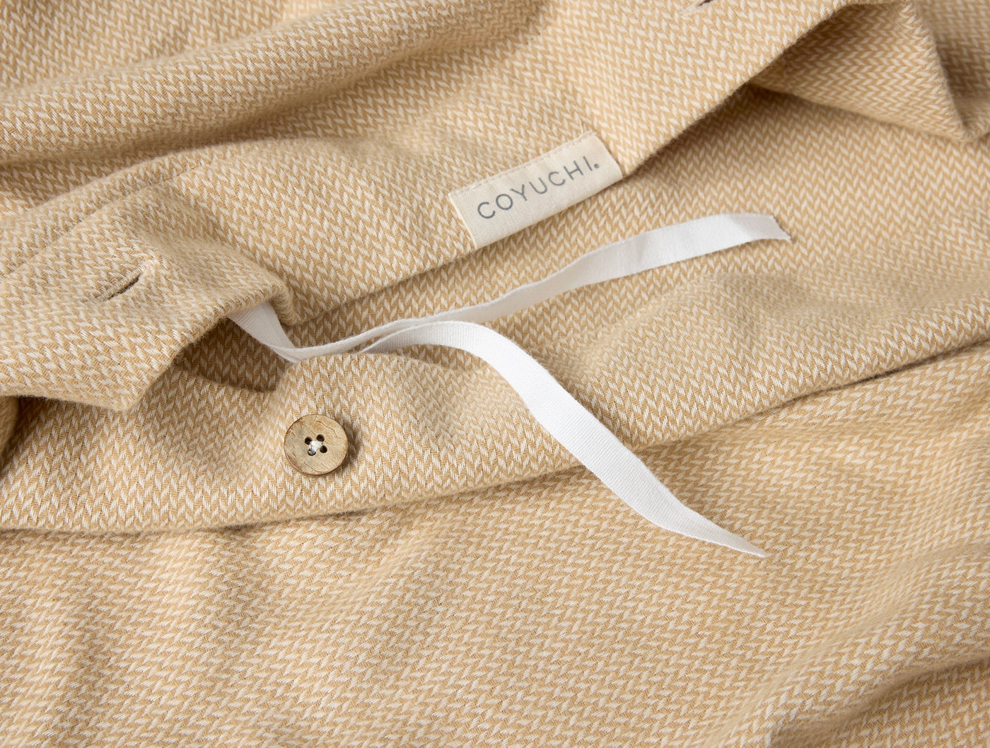 Close-up of Coyuchi duvet cover button closure and woven label on honey herringbone flannel.