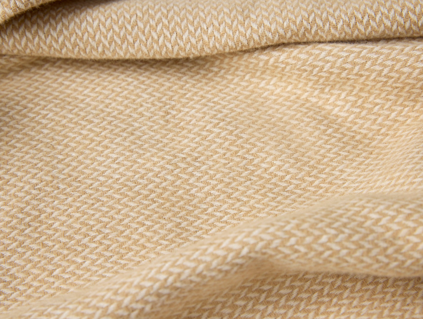Close-up of honey and ivory herringbone weave texture on draped flannel fabric.