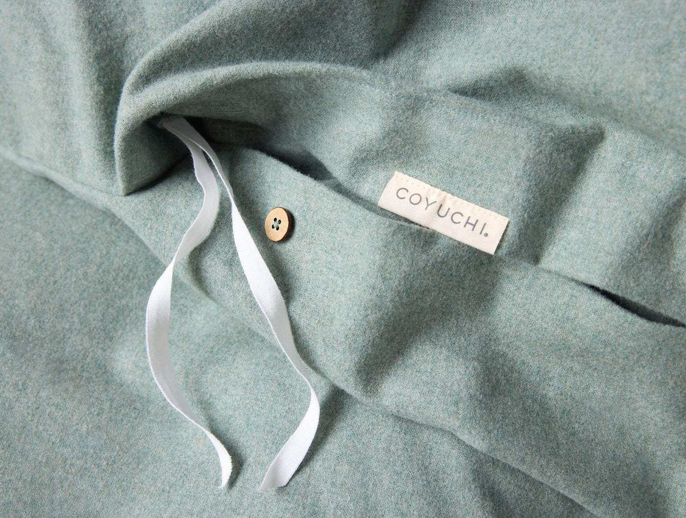 Close-up of Coyuchi duvet cover interior ties and button closure in sage flannel.