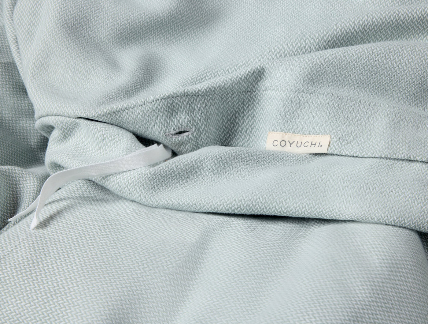 Close-up of Coyuchi woven label on draped sage green flannel duvet cover.