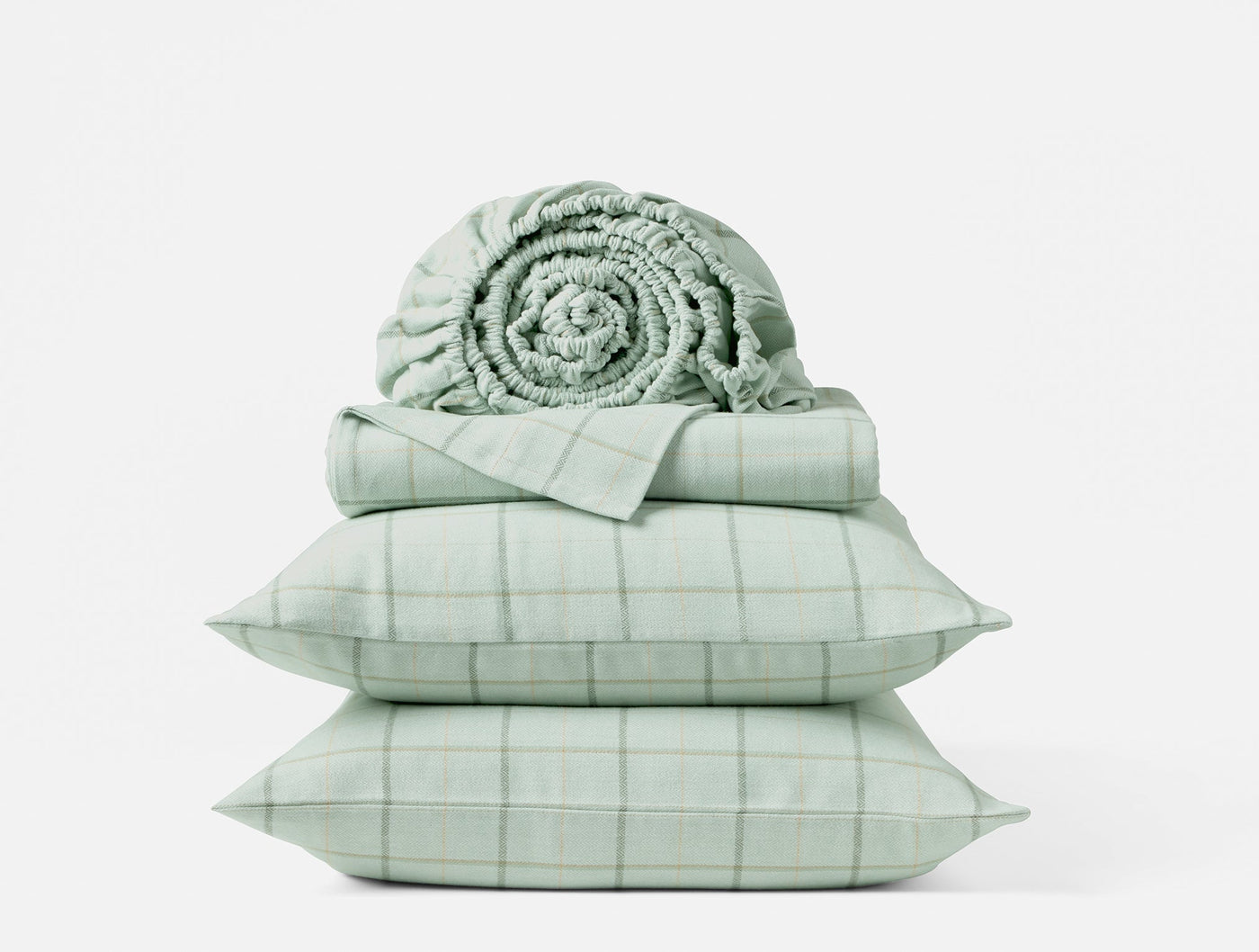 Close-up of sage green plaid flannel sheet set stacked with rolled blanket and two pillowcases.