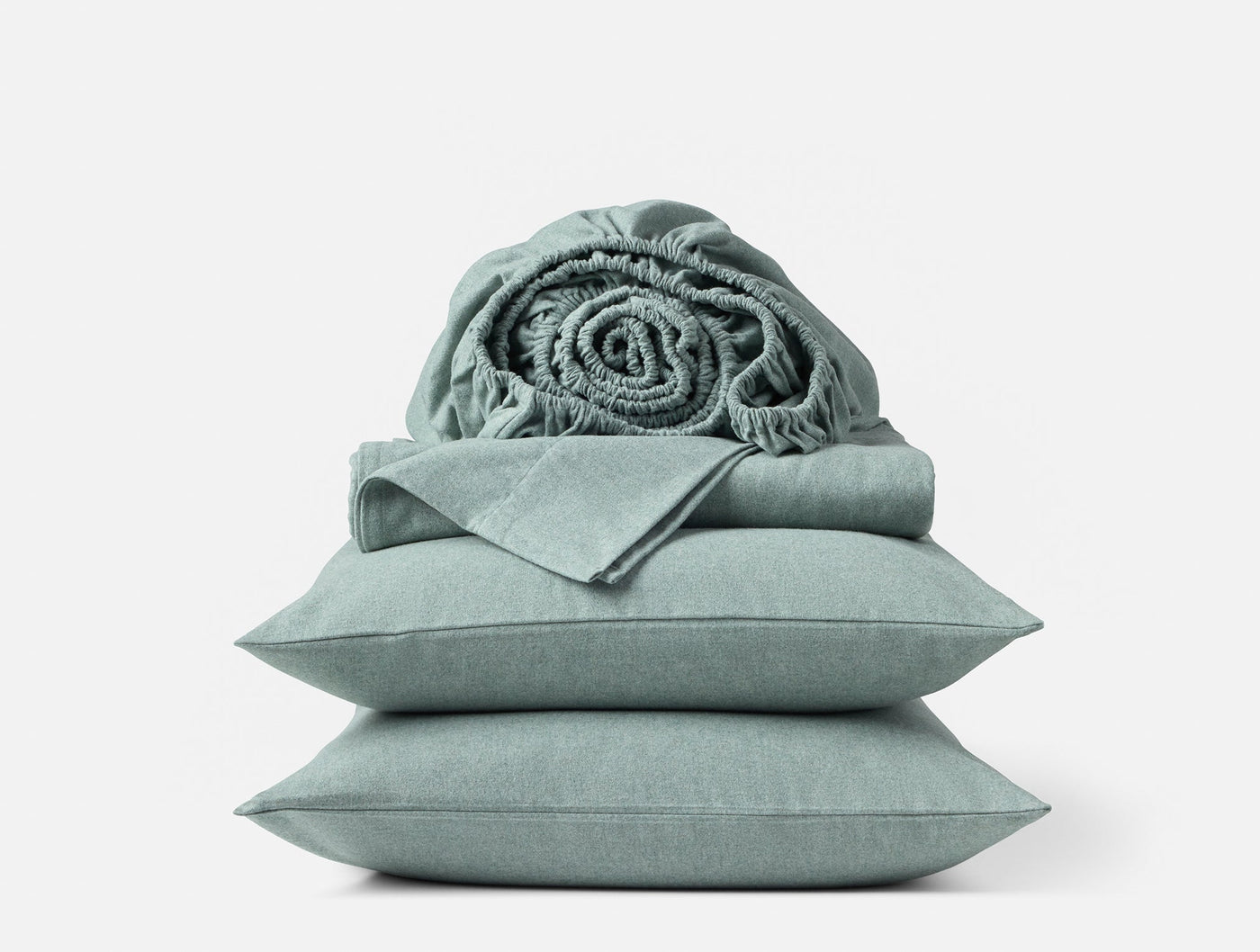 Rolled flannel throw resting atop folded sage green sheets and stacked pillowcases.