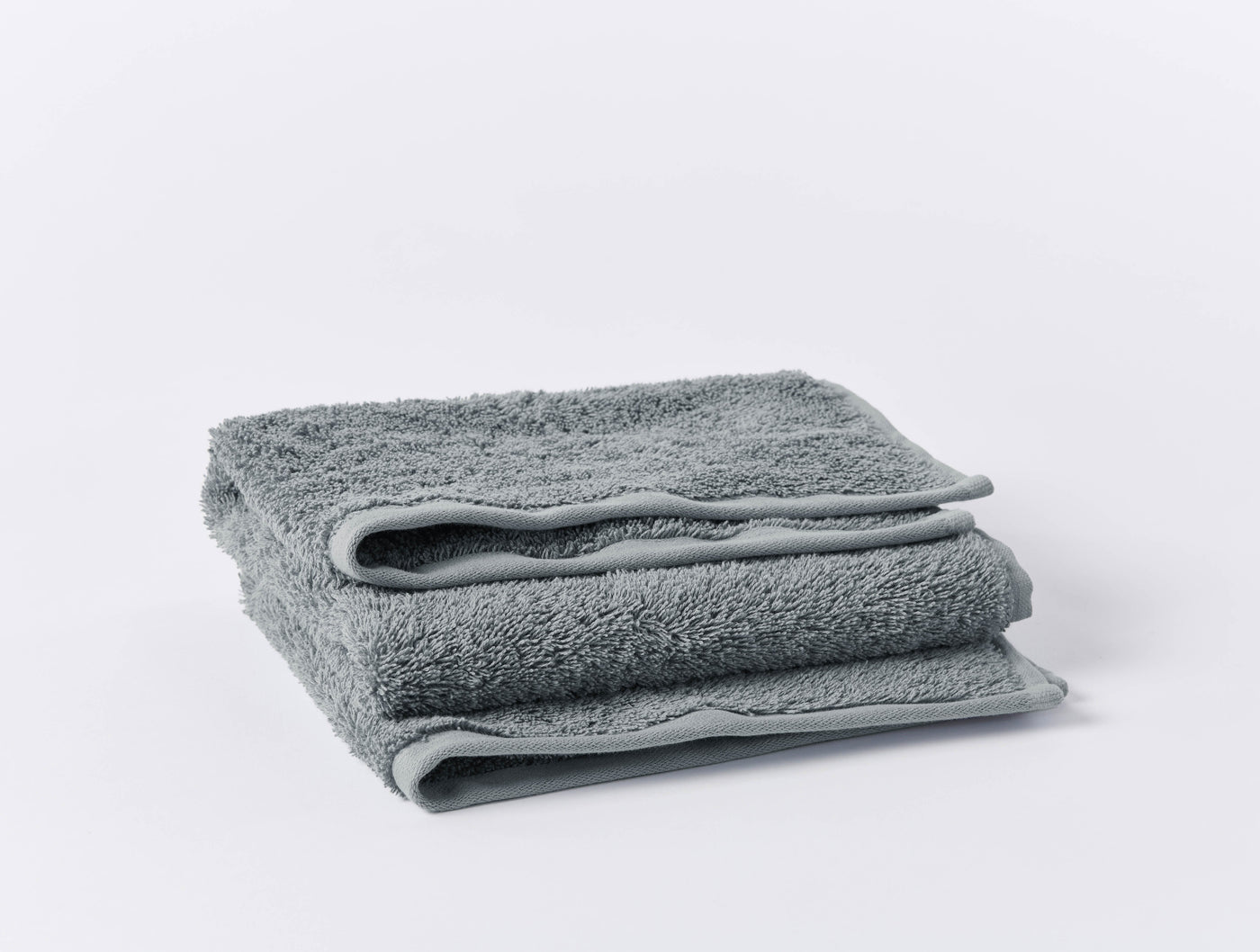 Folded slate grey terry bath towel showing plush loop texture and hemmed edge detail.