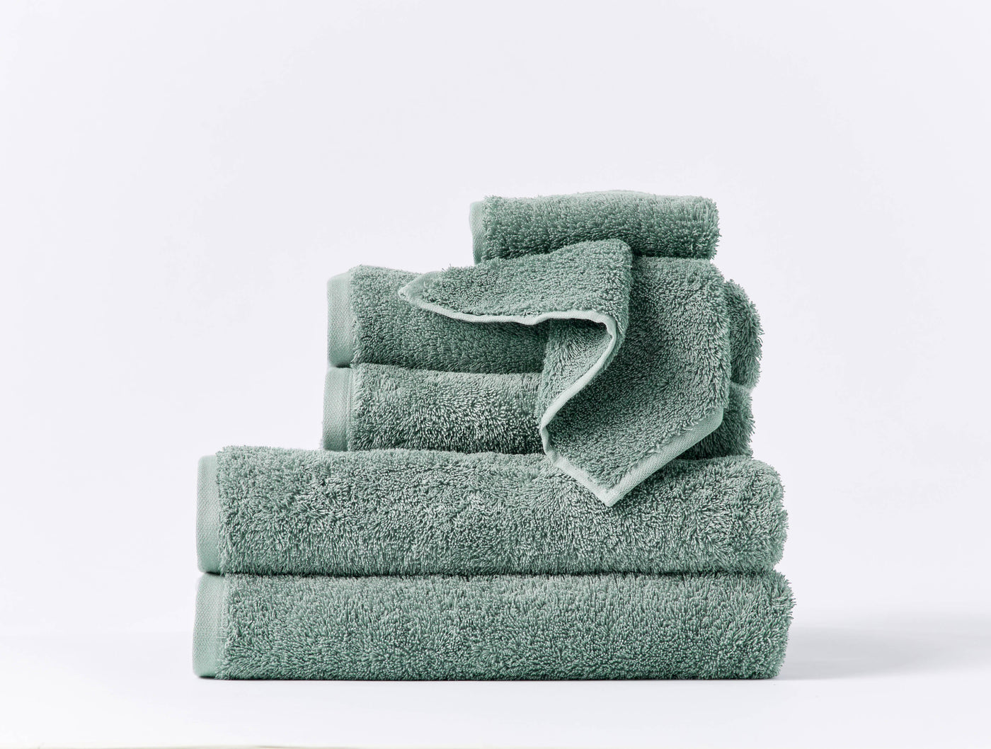 Stacked sage green Coyuchi Cloud Loom towel set showing varied sizes on white background.