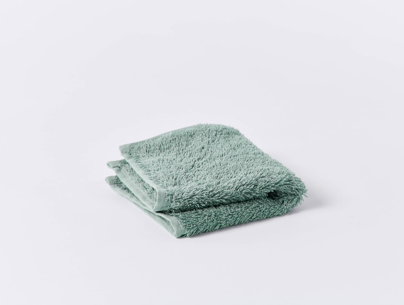 Folded sage green terry washcloth with plush loop texture, shown on white background.