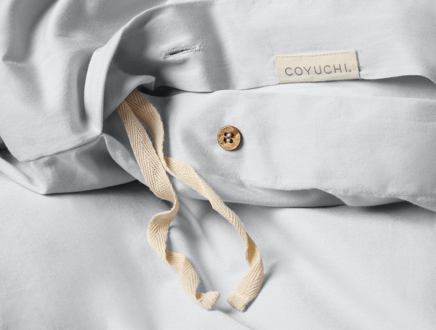 Close-up of Coyuchi duvet cover interior ties, coconut button, and woven label on white sateen.