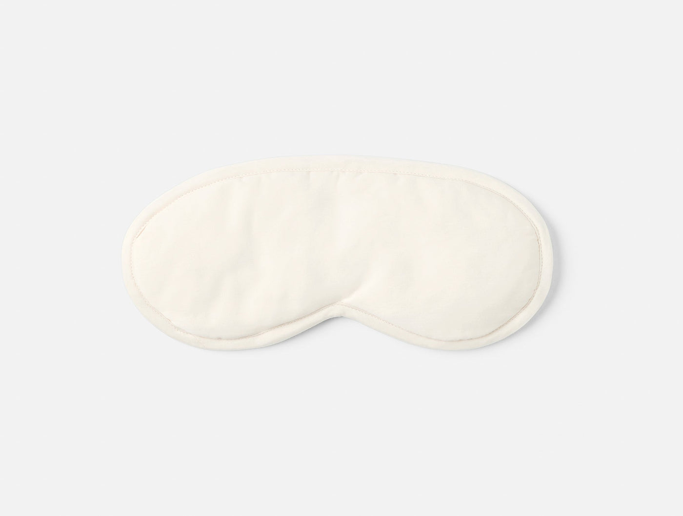 Ivory sateen eye mask shown from above on a light grey background.