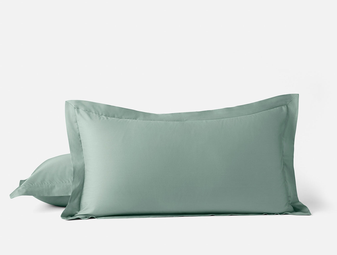 Close-up of two sage green Coyuchi Cloud Soft Sateen pillow shams stacked against white background.