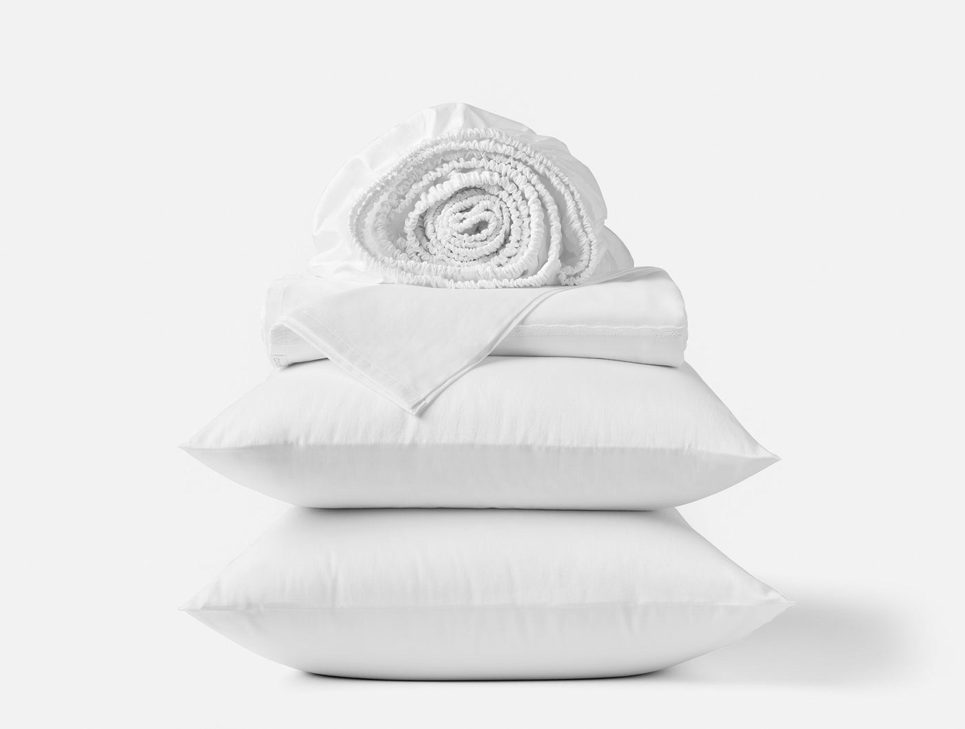 Stacked white Coyuchi Cloud Soft Sateen sheet set with rolled blanket atop two pillows.