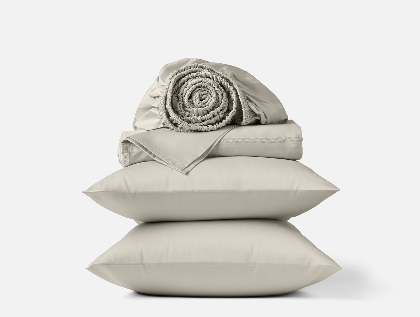 Stacked Coyuchi pillowcases in pebble with rolled sateen sheet set on top.