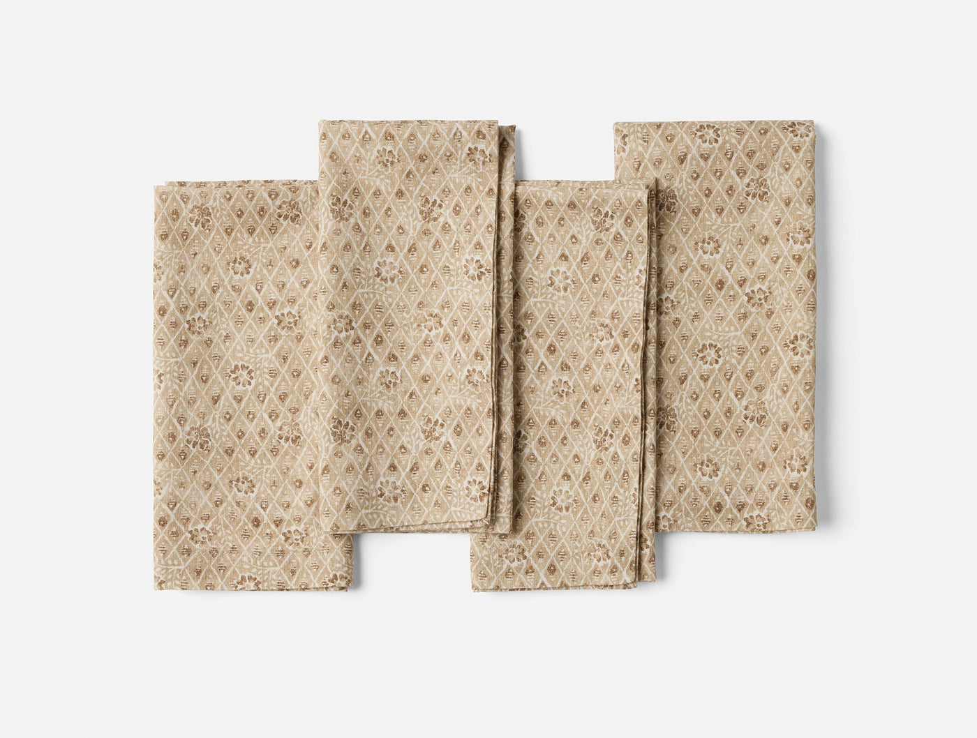 Close-up of four folded Coyuchi Coral Bell Print napkins in tan with floral diamond pattern.