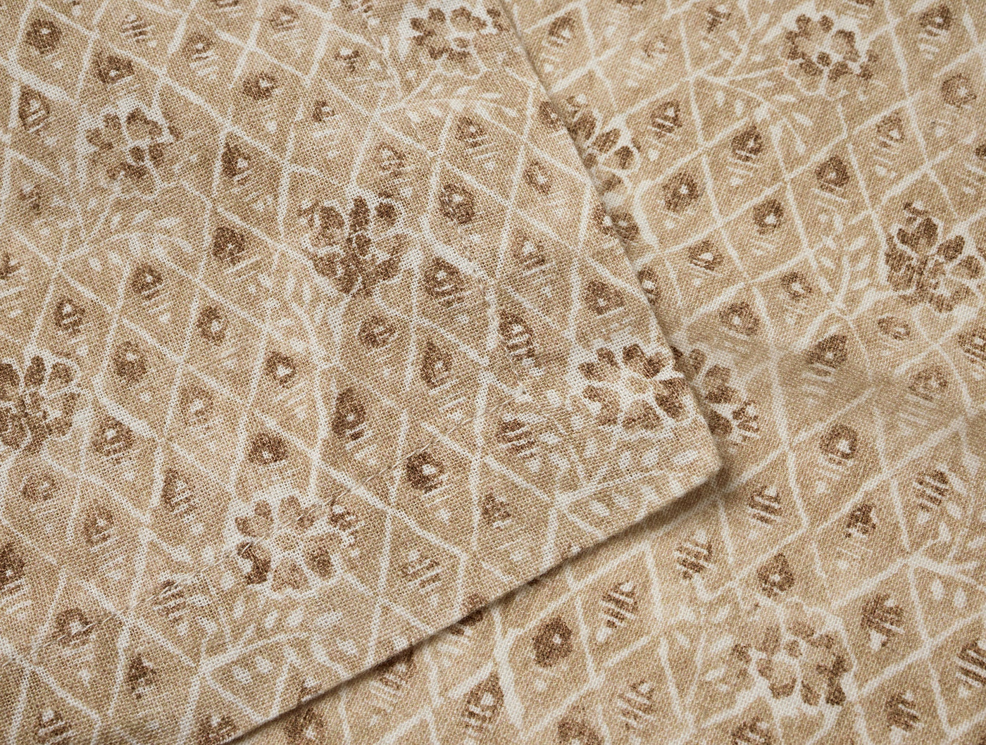 Close-up of Coyuchi Coral Bell Print napkins, champagne diamond and floral pattern, folded edge detail.
