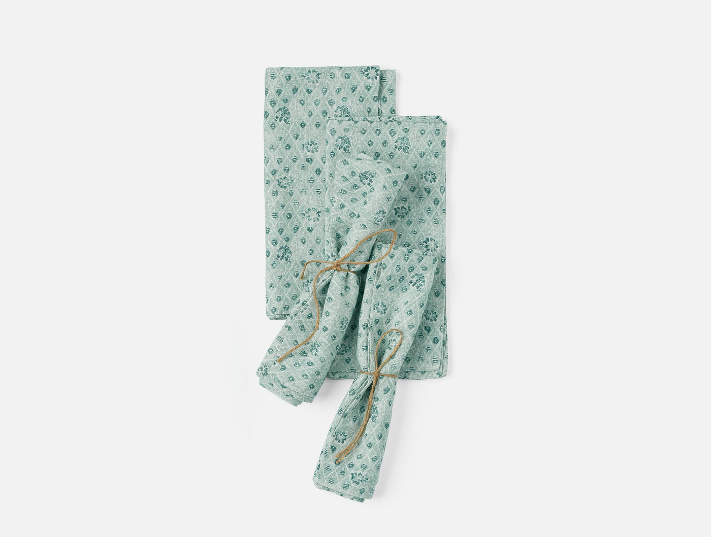 Coyuchi Coral Bell Print napkins in sage green, two folded and one tied with twine.