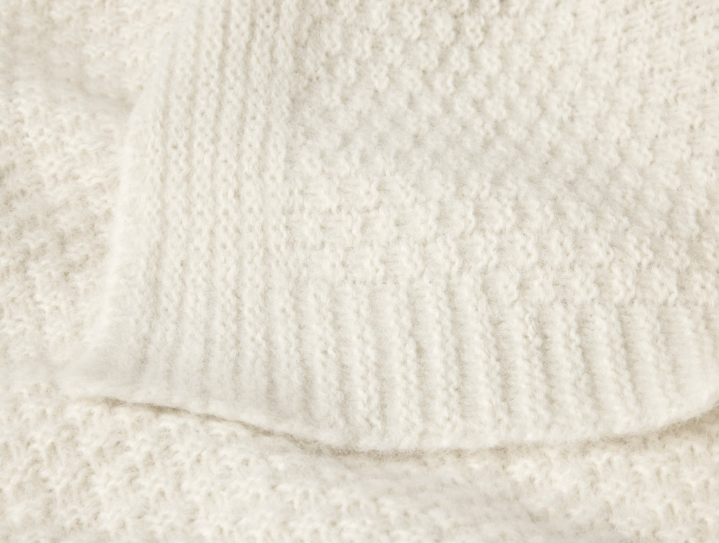 Close-up of ivory alpaca cotton knit throw hem, showing ribbed border and textured weave detail.