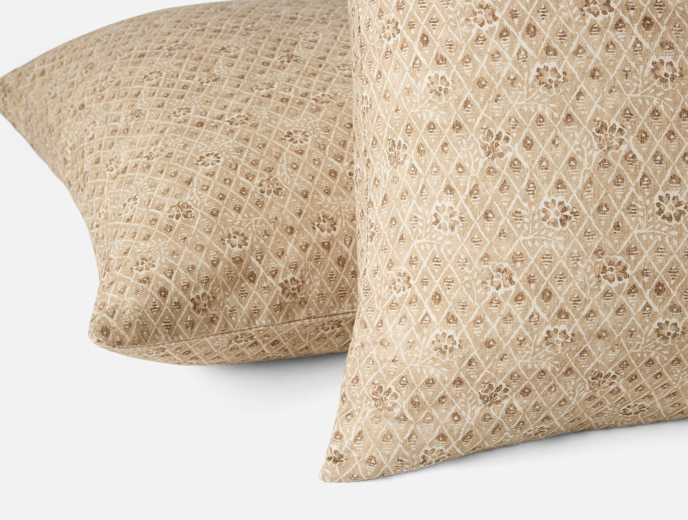 Close-up of two Coyuchi Coral Bell Print pillow covers in champagne with diamond lattice floral pattern.