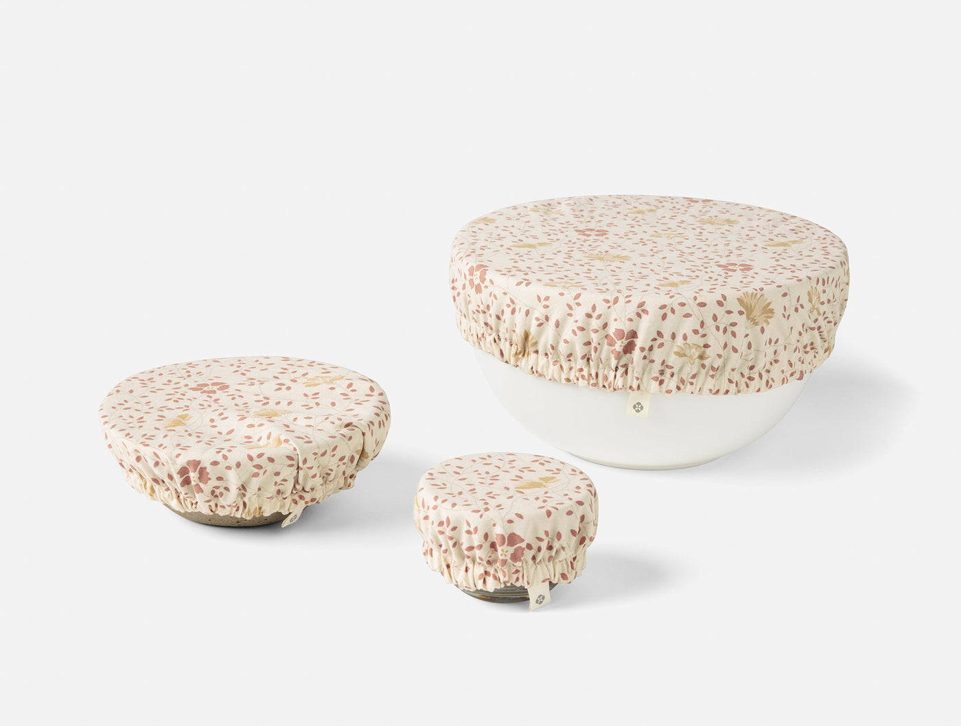 Three Coyuchi Conserve bowl covers in varied sizes, ivory with scattered floral print.