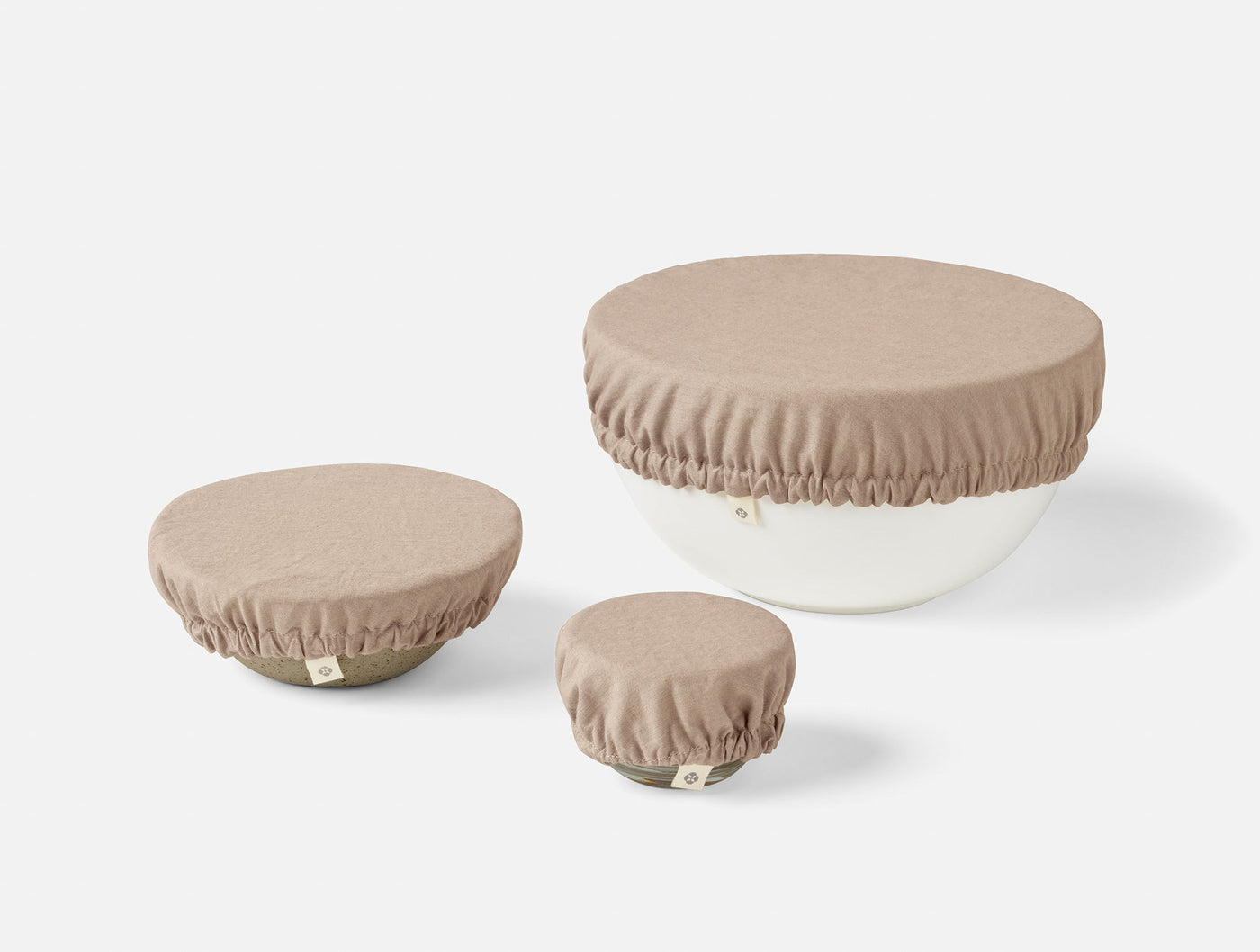 Three Coyuchi linen bowl covers in warm taupe, shown in small, medium, and large sizes.