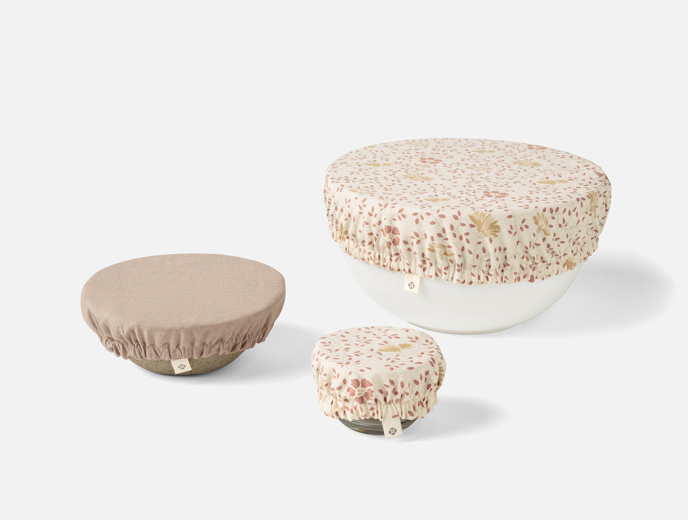 Close-up of three Coyuchi Conserve bowl covers: two floral print, one taupe, in small, medium, large sizes.